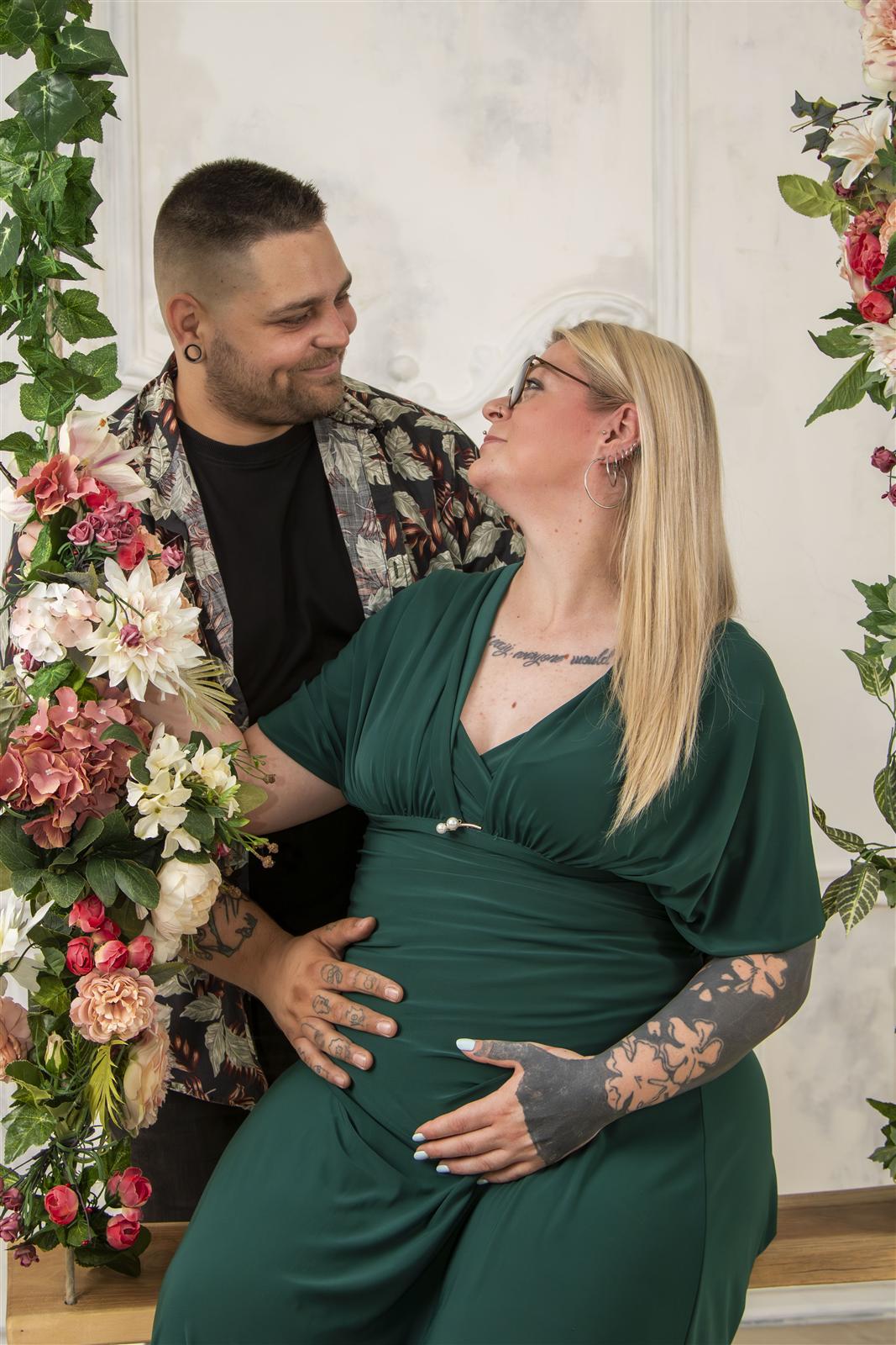 Kismama és párja zöld ruhában, virágos háttér előtt